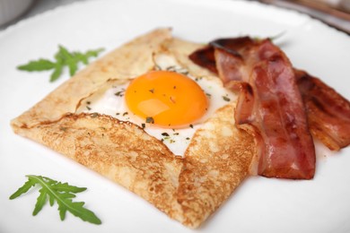 Photo of Delicious crepe with egg on white plate, closeup. Breton galette