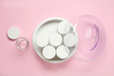 Modern yogurt maker with jars on pink background, flat lay