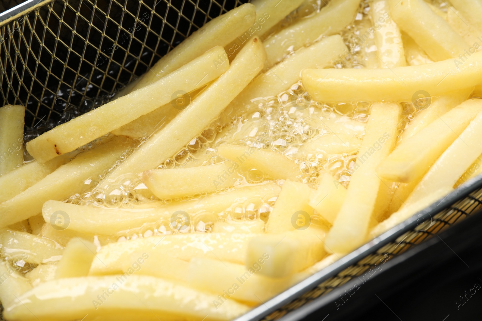 Photo of Cooking delicious french fries in hot oil, closeup