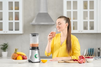 Photo of Beautiful young woman with delicious smoothie in kitchen