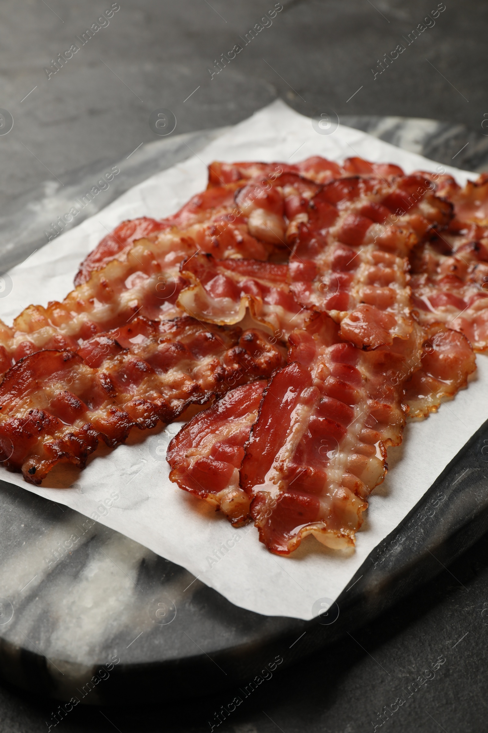 Photo of Fried bacon slices on dark table, closeup