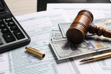 Photo of Tax return forms, dollar banknotes, gavel, calculator and pen on table, closeup