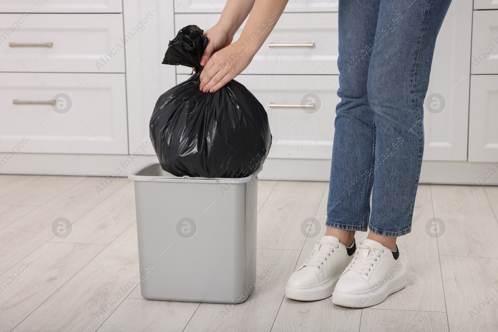 Photo of Woman taking garbage bag out of trash bin in kitchen, closeup