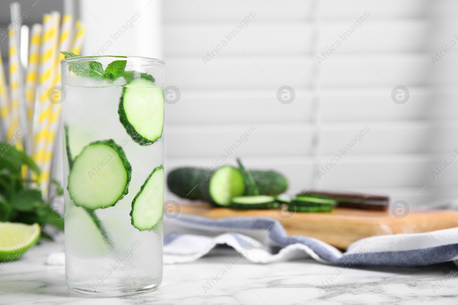 Photo of Glass of refreshing cucumber water with mint on white marble table, space for text