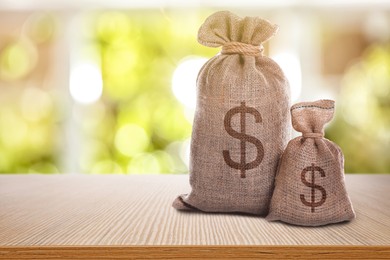 Image of Burlap bags with dollar signs on wooden table indoors. Space for text