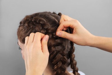 Professional stylist braiding woman's hair on grey background, closeup