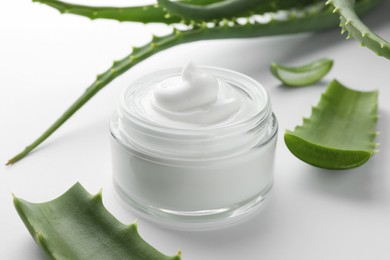 Jar of natural cream and aloe leaves on white background, closeup