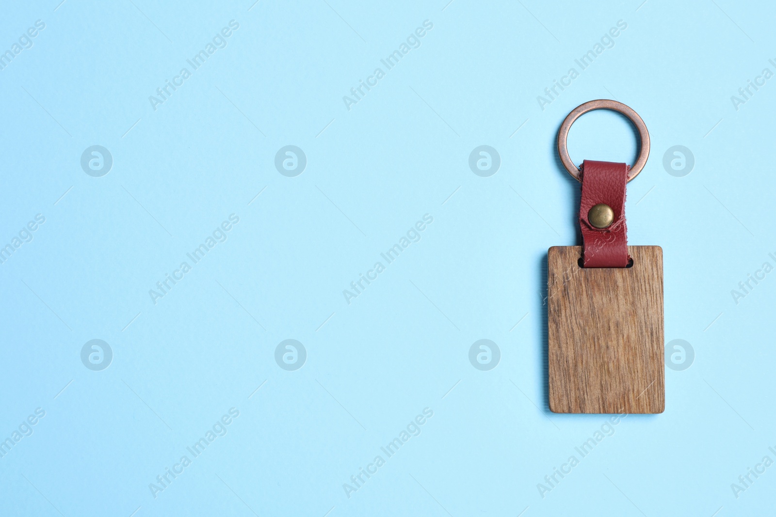 Photo of Wooden keychain with Ukrainian coat of arms on light blue background, top view. Space for text