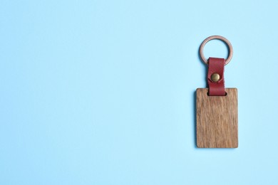 Photo of Wooden keychain with Ukrainian coat of arms on light blue background, top view. Space for text