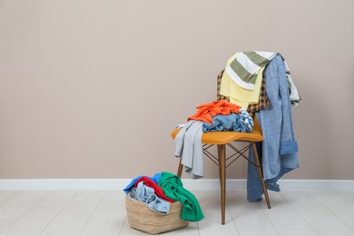 Photo of Orange chair and wicker basket with different clothes near light grey wall, space for text