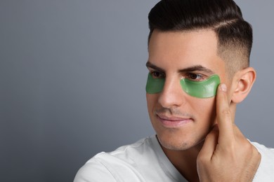 Man applying green under eye patch on grey background. Space for text