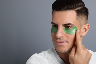 Photo of Man applying green under eye patch on grey background. Space for text