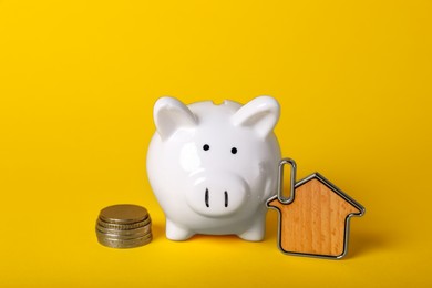 Photo of Ceramic piggy bank, coins and key trinket on yellow background. Financial savings