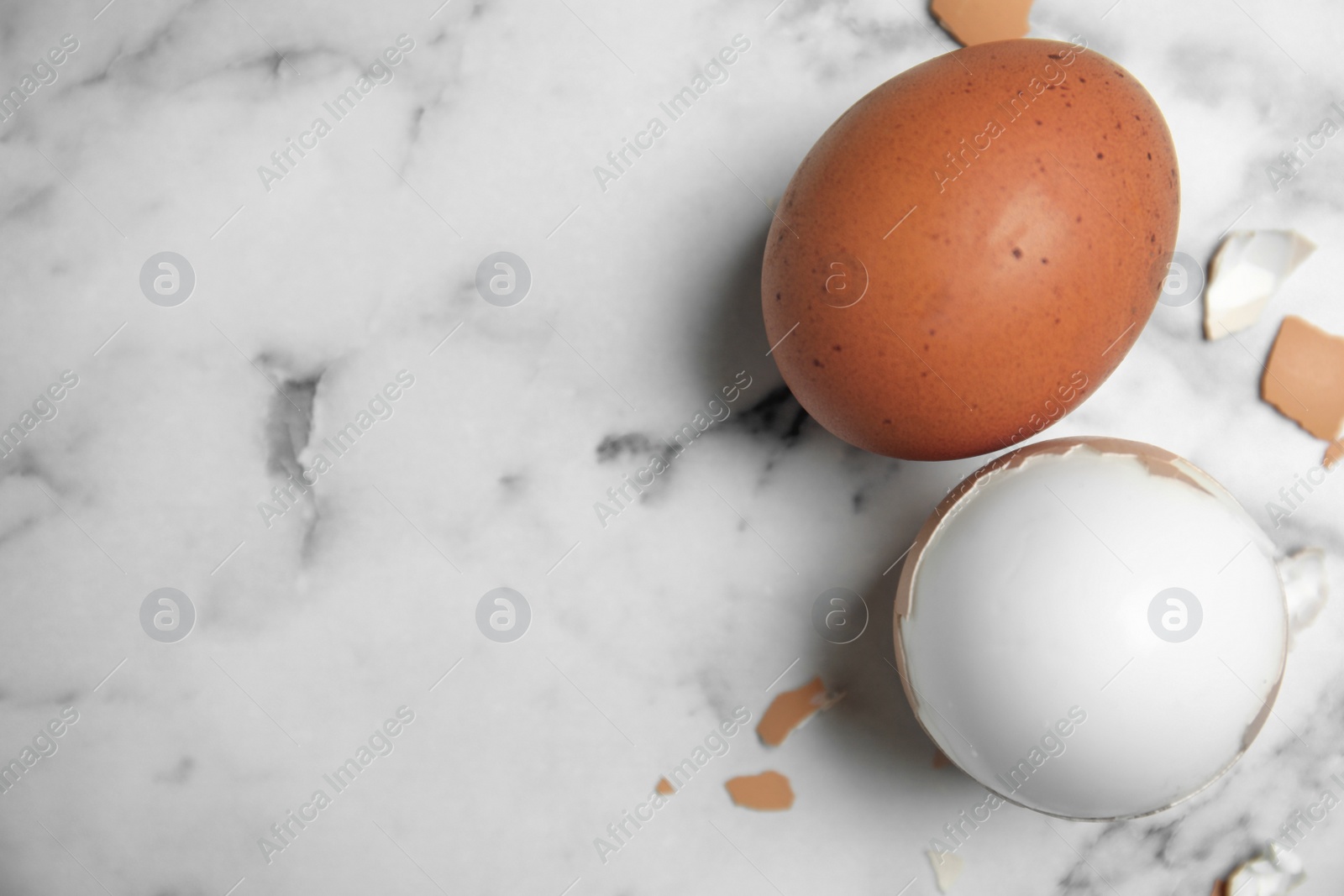 Photo of Boiled eggs and pieces of shell on white marble table, flat lay. Space for text