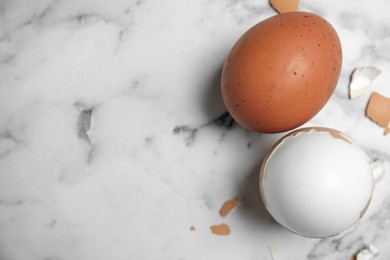 Boiled eggs and pieces of shell on white marble table, flat lay. Space for text