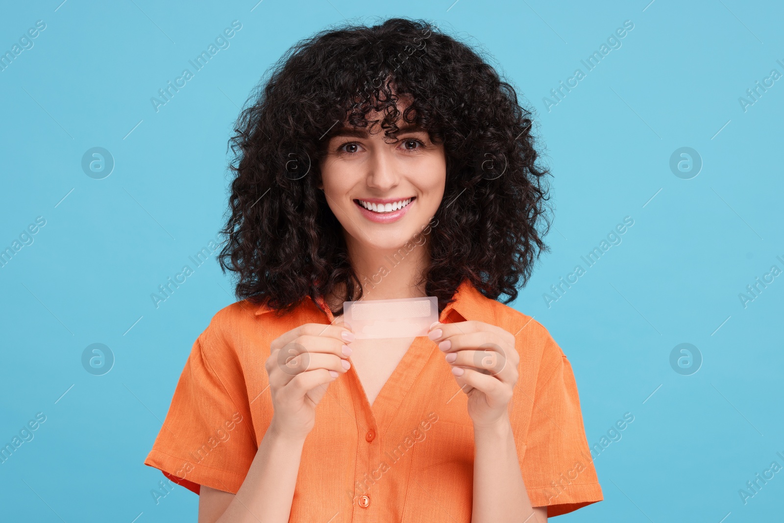 Photo of Young woman holding teeth whitening strips on light blue background