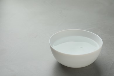 Photo of White bowl with water on grey table. Space for text