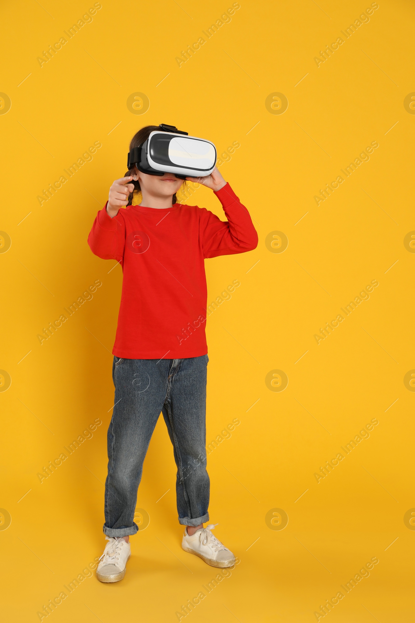 Photo of Little girl using virtual reality headset on yellow background