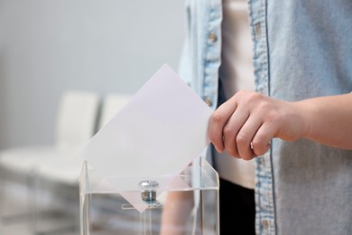 Photo of Woman putting her vote into ballot box on blurred background, closeup