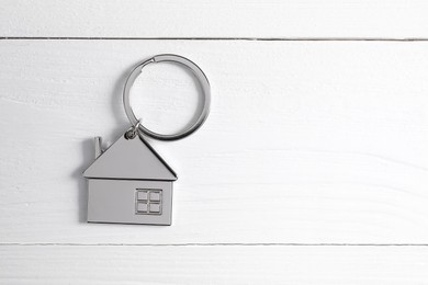 Photo of Metal keychain in shape of house on white wooden table, top view. Space for text