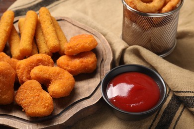 Tasty ketchup, chicken nuggets and cheese sticks on beige tablecloth, closeup