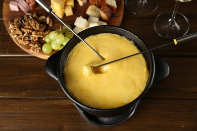 Photo of Fondue pot with melted cheese and different products on wooden table, above view