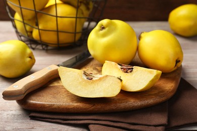 Photo of Ripe whole and cut quinces with knife on wooden table, closeup