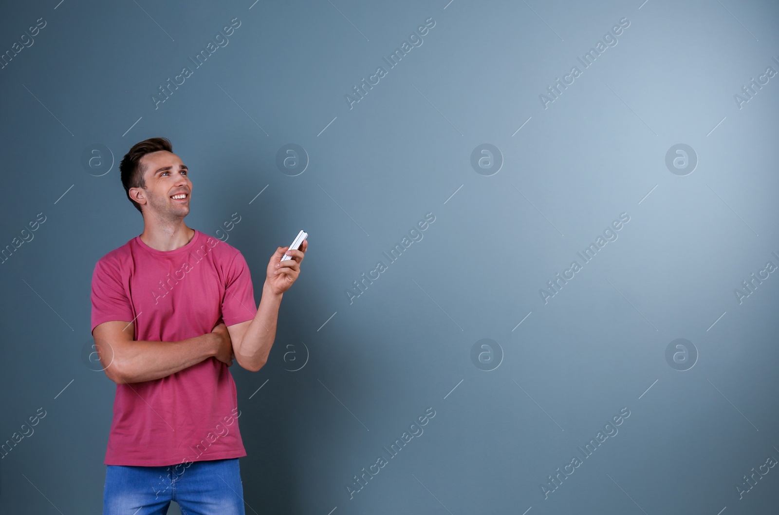 Photo of Happy young man operating air conditioner with remote control on dark background