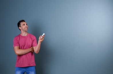 Photo of Happy young man operating air conditioner with remote control on dark background