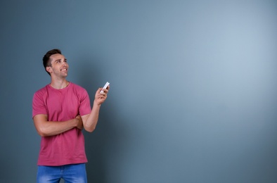 Happy young man operating air conditioner with remote control on dark background