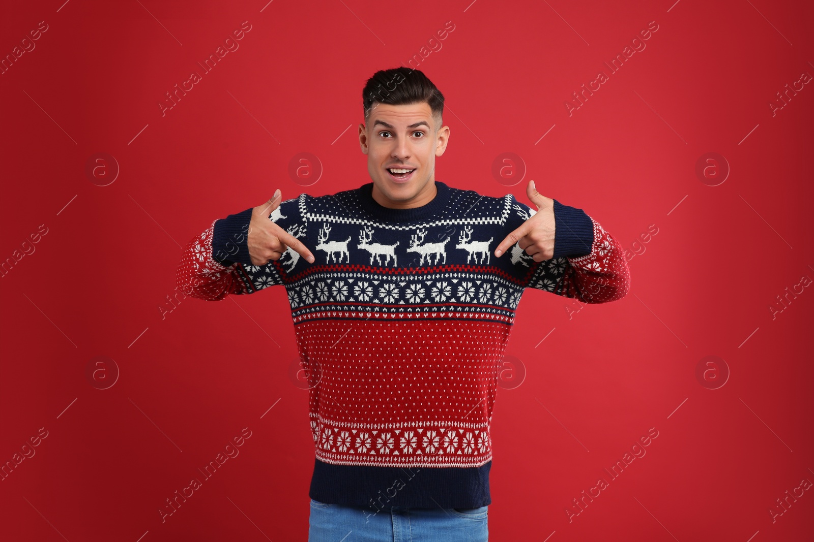Photo of Handsome man pointing on his Christmas sweater against red background