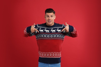 Photo of Handsome man pointing on his Christmas sweater against red background