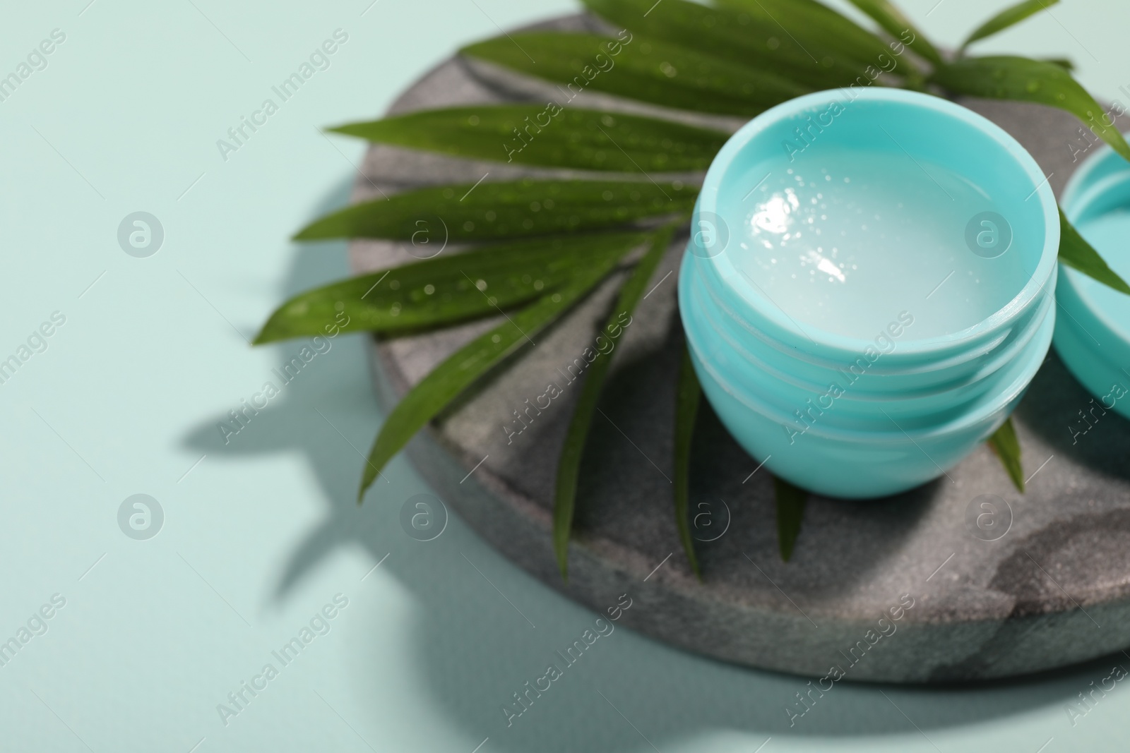 Photo of Lip balm and palm leaf on light blue background, closeup. Space for text