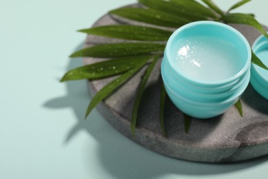 Photo of Lip balm and palm leaf on light blue background, closeup. Space for text