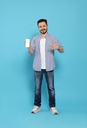 Smiling man pointing at smartphone on light blue background