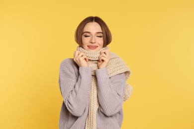 Photo of Beautiful young woman in scarf and sweater on yellow background. Winter season