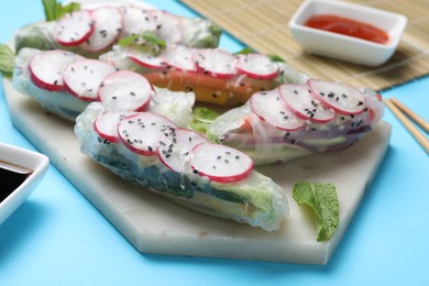 Photo of Delicious spring rolls and mint on light blue background