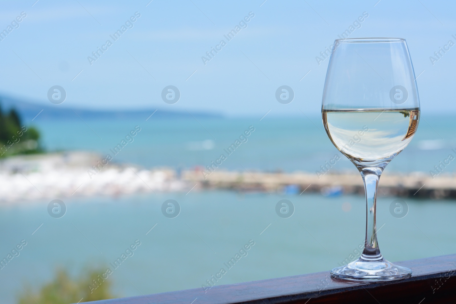 Photo of Glass with wine on railing near sea. Space for text