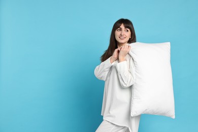 Photo of Happy woman in pyjama holding pillow on light blue background, space for text