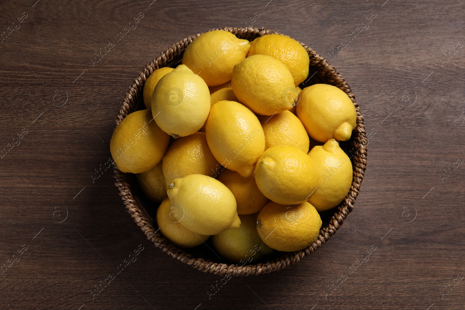 Photo of Fresh lemons in wicker basket on wooden table, top view