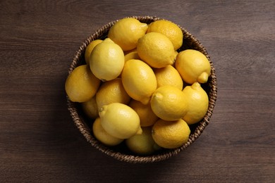 Fresh lemons in wicker basket on wooden table, top view