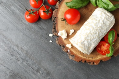 Photo of Delicious fresh goat cheese with tomatoes and basil on grey table, flat lay. Space for text