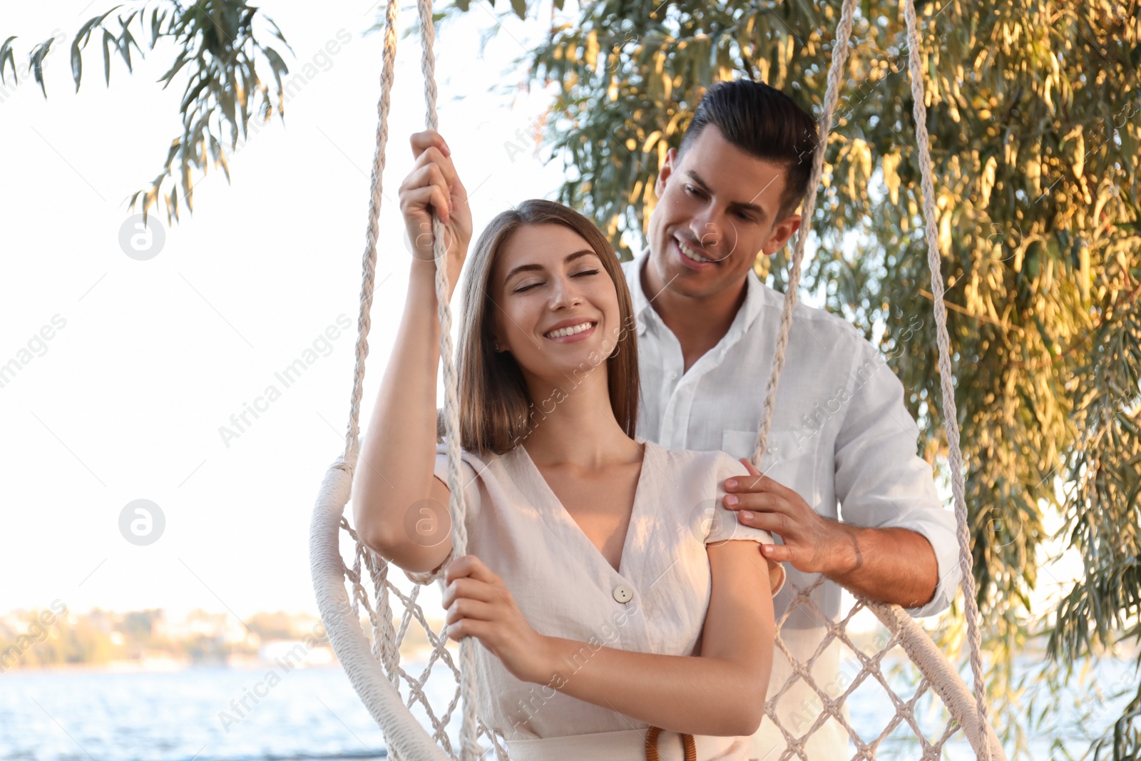 Photo of Young woman in hammock chair and her boyfriend on beach. Summer vacation