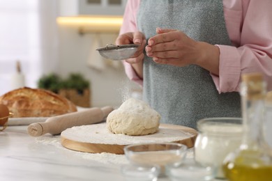 Making bread. Woman sifting flour onto dough at white table in kitchen, closeup