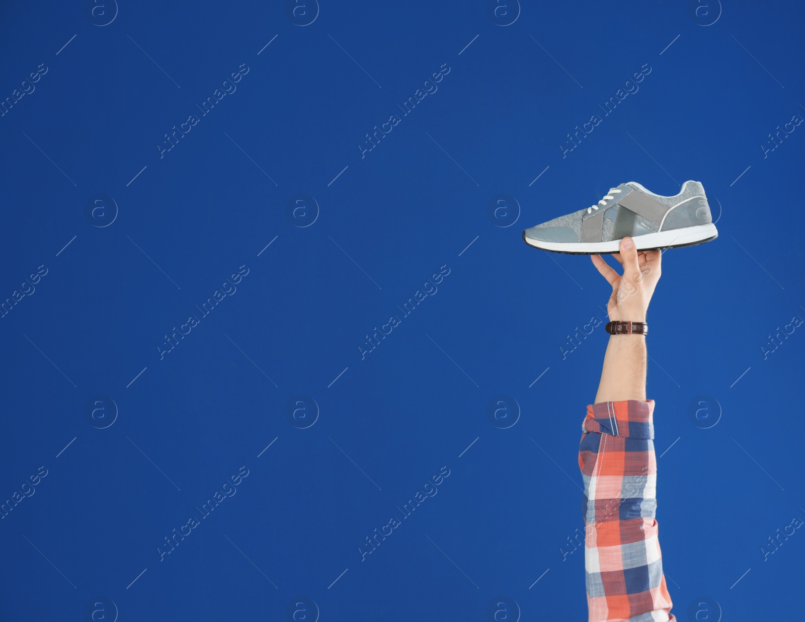 Photo of Young man holding comfortable shoe on blue background, closeup. Space for text