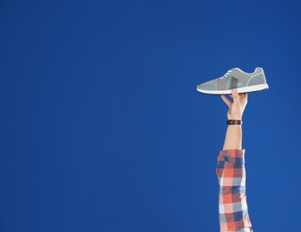 Photo of Young man holding comfortable shoe on blue background, closeup. Space for text