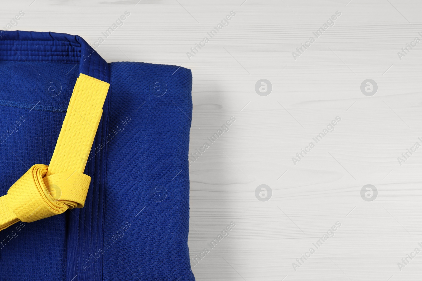 Photo of Yellow karate belt and blue kimono on wooden background, top view. Space for text