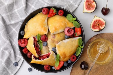 Bowl with delicious samosas, berries, fig, honey and mint leaves on white tiled table, flat lay