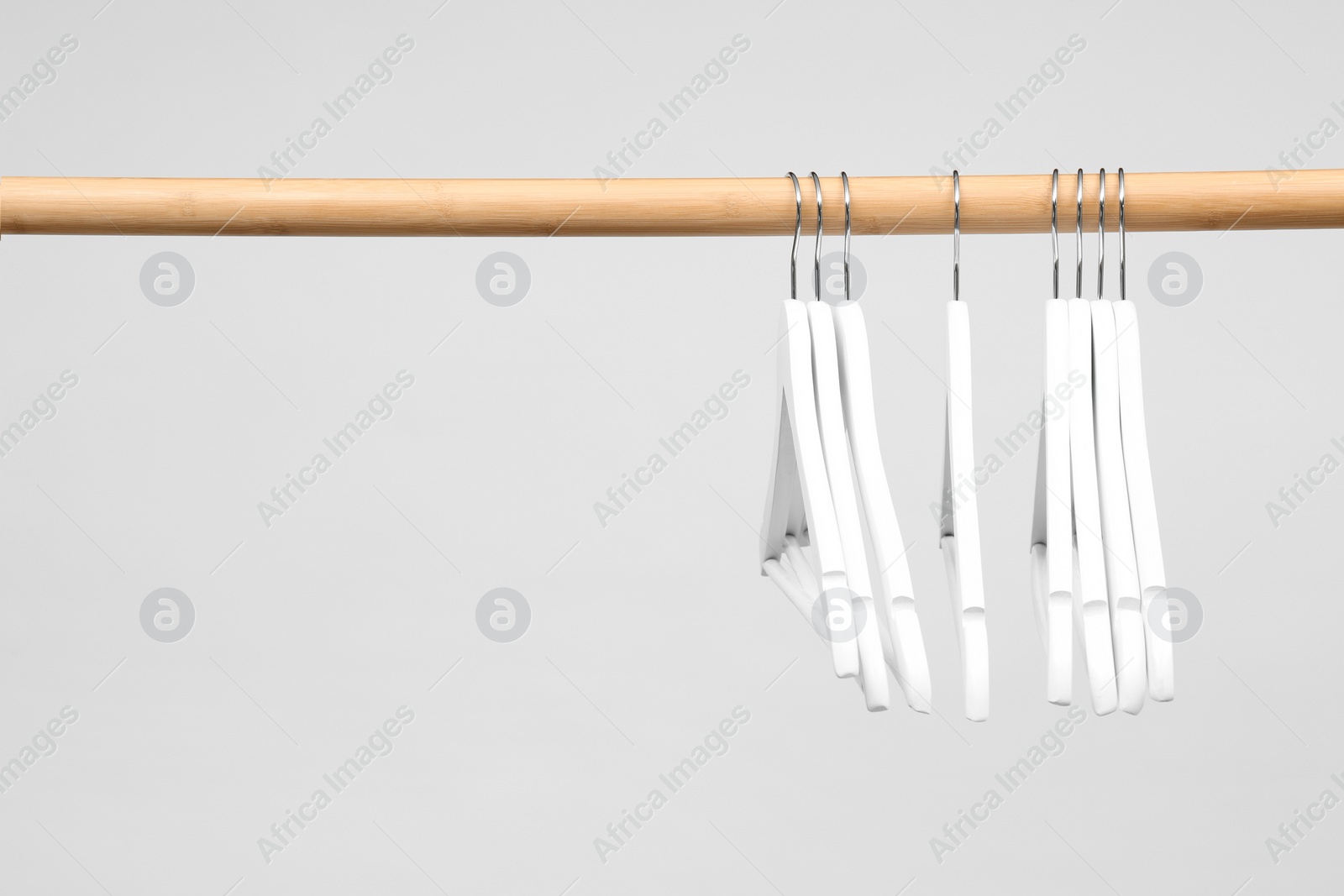 Photo of Empty clothes hangers on wooden rail against light background. Space for text