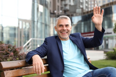 Photo of Portrait of handsome mature man sitting on bench in city center